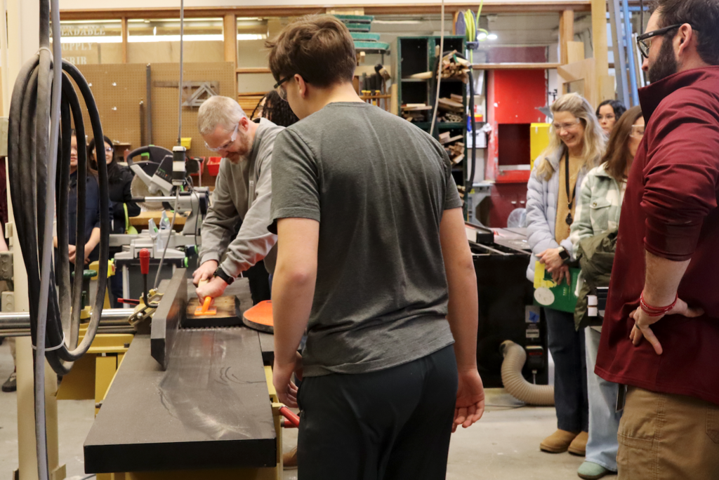 student watching someone run wood through the machine