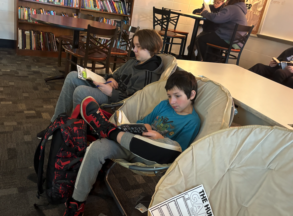 two boys sitting in chairs reading books at tables