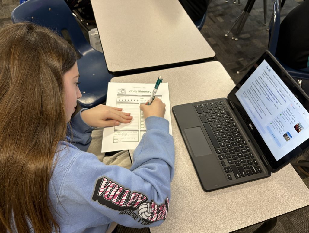 student writing on paper with computer