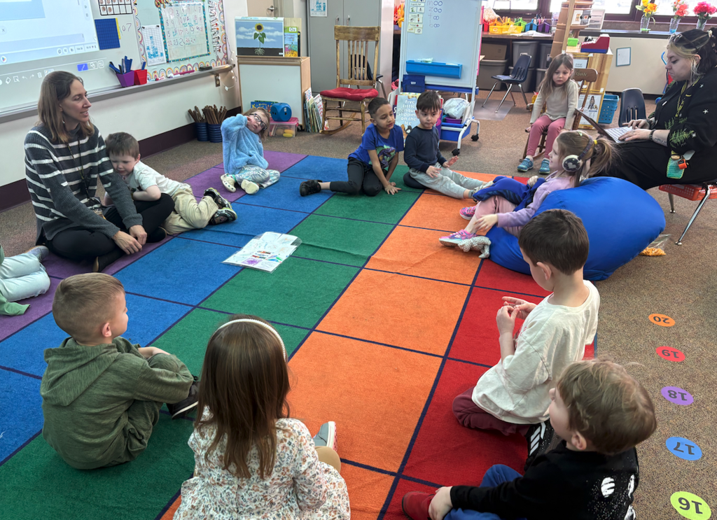 class sitting around in a circle with teacher on floor