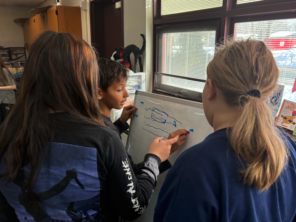 group of three kids working on white boards