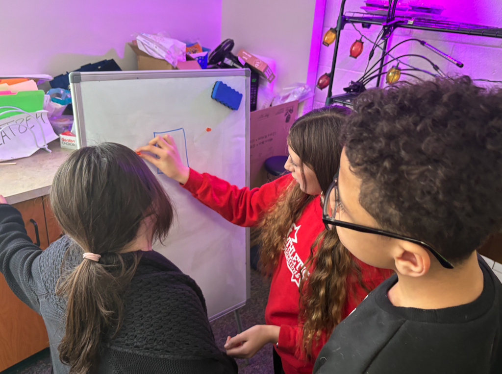 group of three kids working on white boards