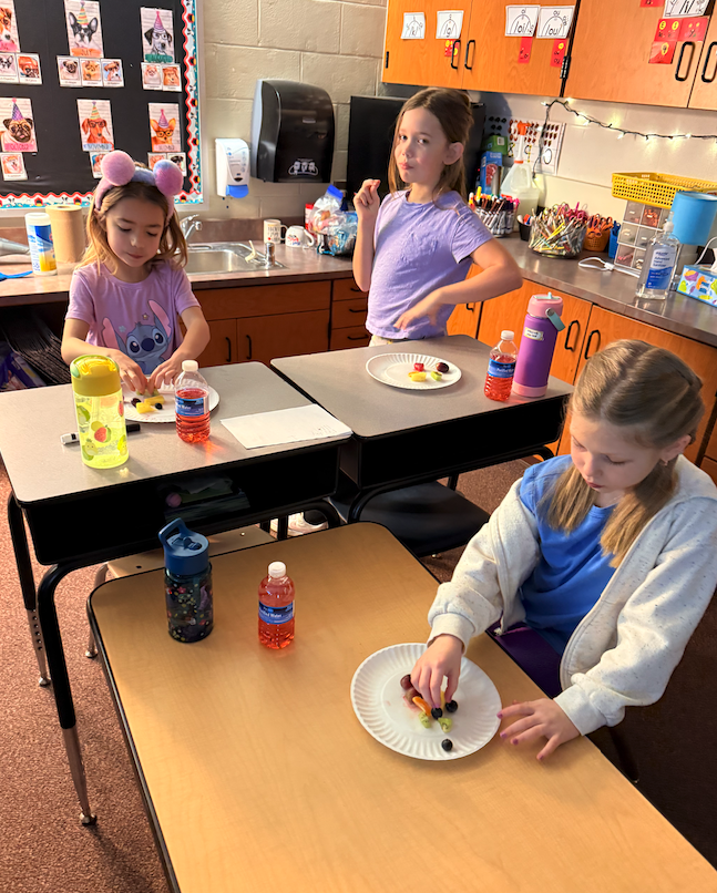 three girls sitting at desk eating fruits