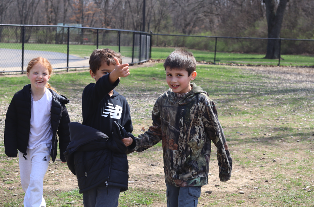 two little boys, with one pointing, and one little girl walking on playground