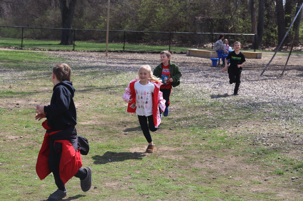 four young elementary children running on the playground at recess