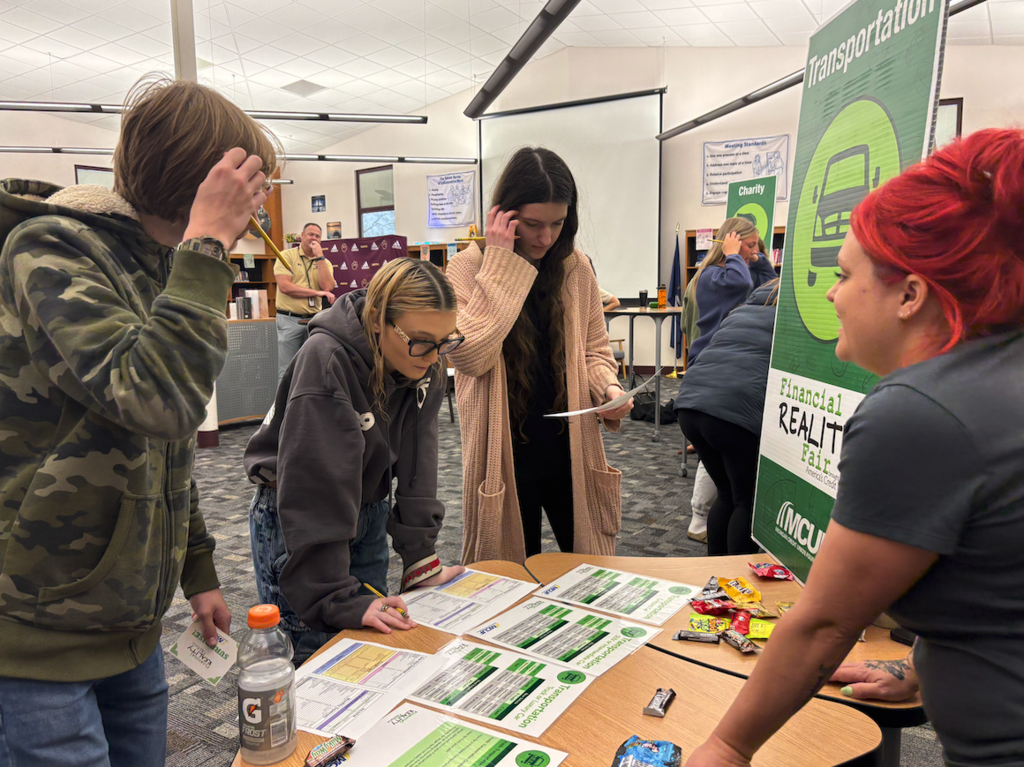 three students standing at table with budget sheets for transportation expenses