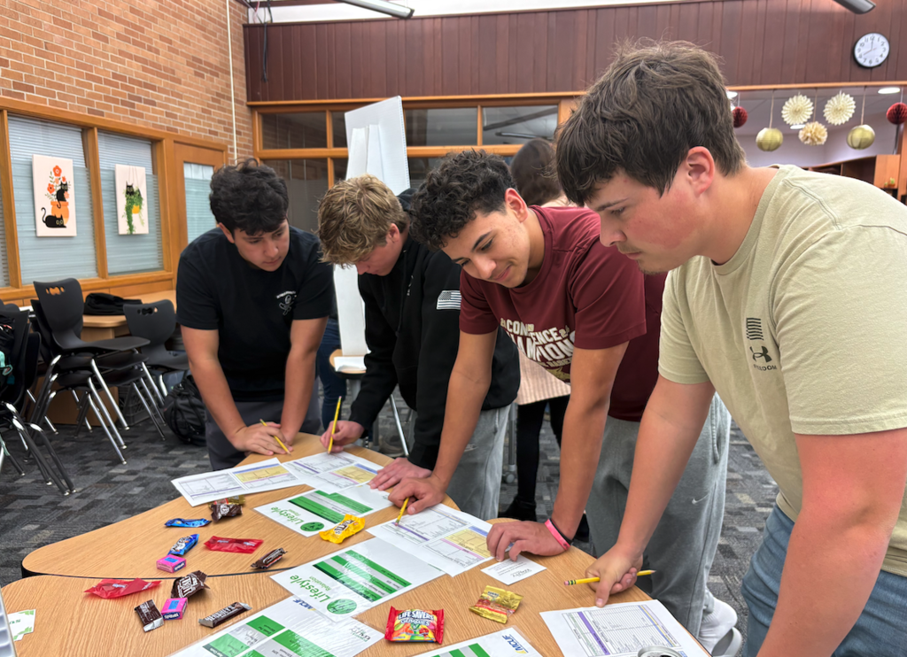 four high school boys standing around table looking at budget sheets