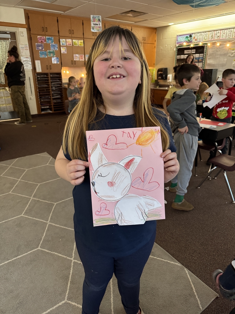 young girl holding picture of bunny picture up in classroom