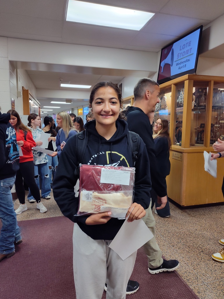 female senior with brown hair holding package of cap and gown