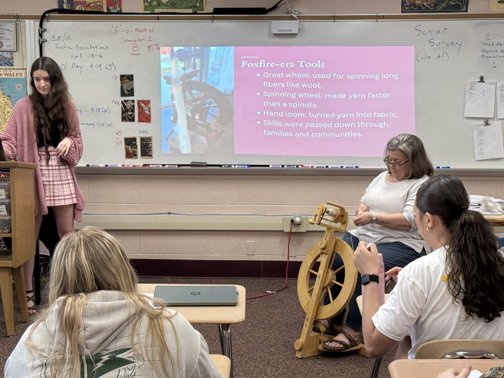 student presenting to class while teacher weaves next to her