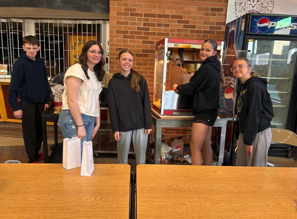 group of four girls making popcorn with young man, selling popcorn in the cafeteria