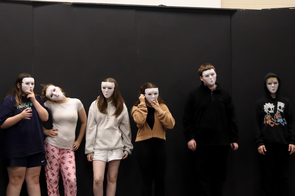 students standing on stage with white masks on 