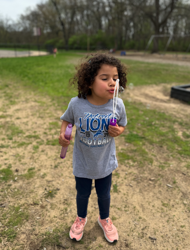 little girl with curly hair blowing bubbles on the playground