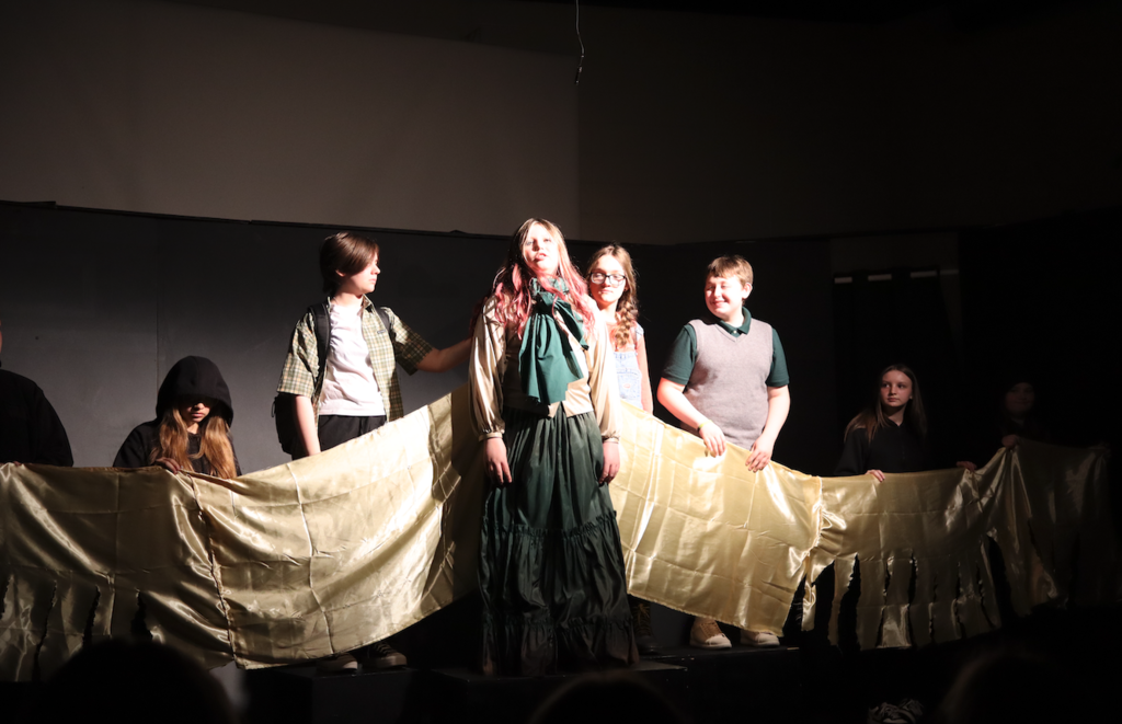 actors holding up train of actress's dress on stage