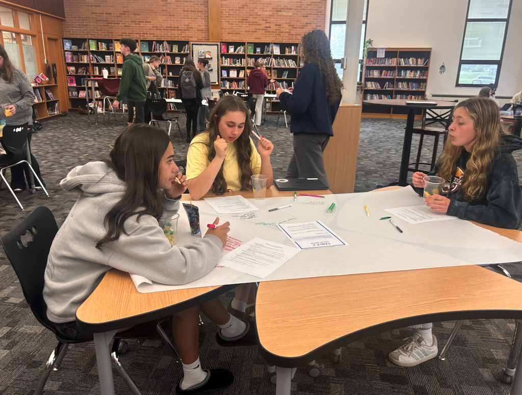 three young ladies sitting at a table discussing and writing