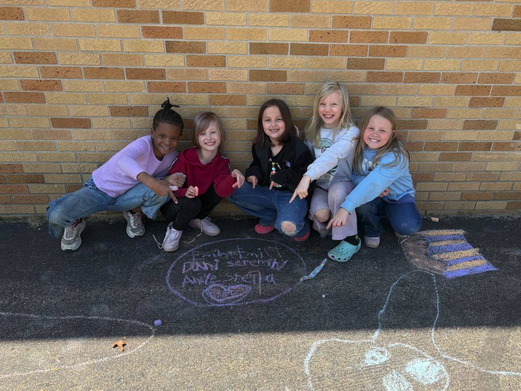 five little girls sitting on ground, pointing at chalk drawing