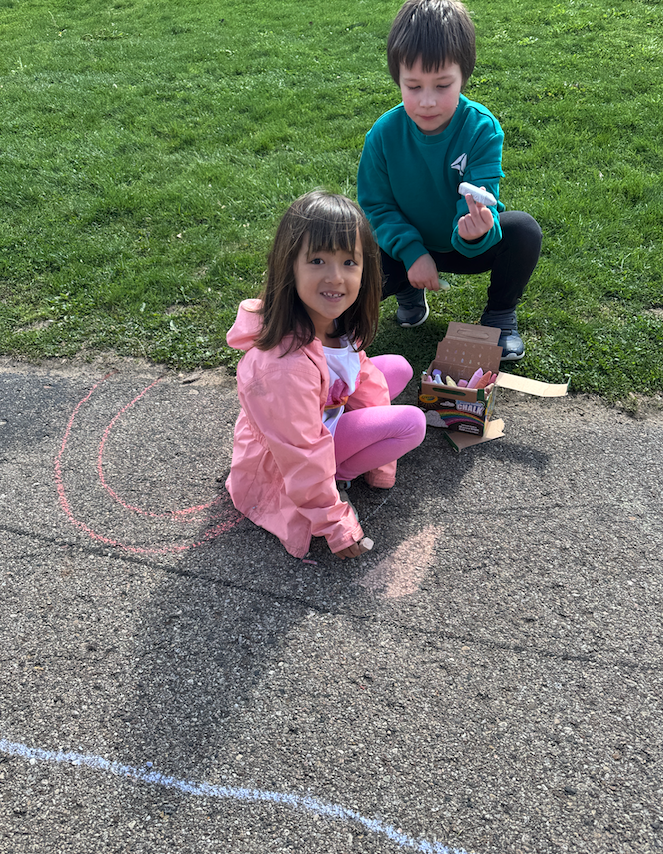 little girl with little boy drawing on pavement with chalk