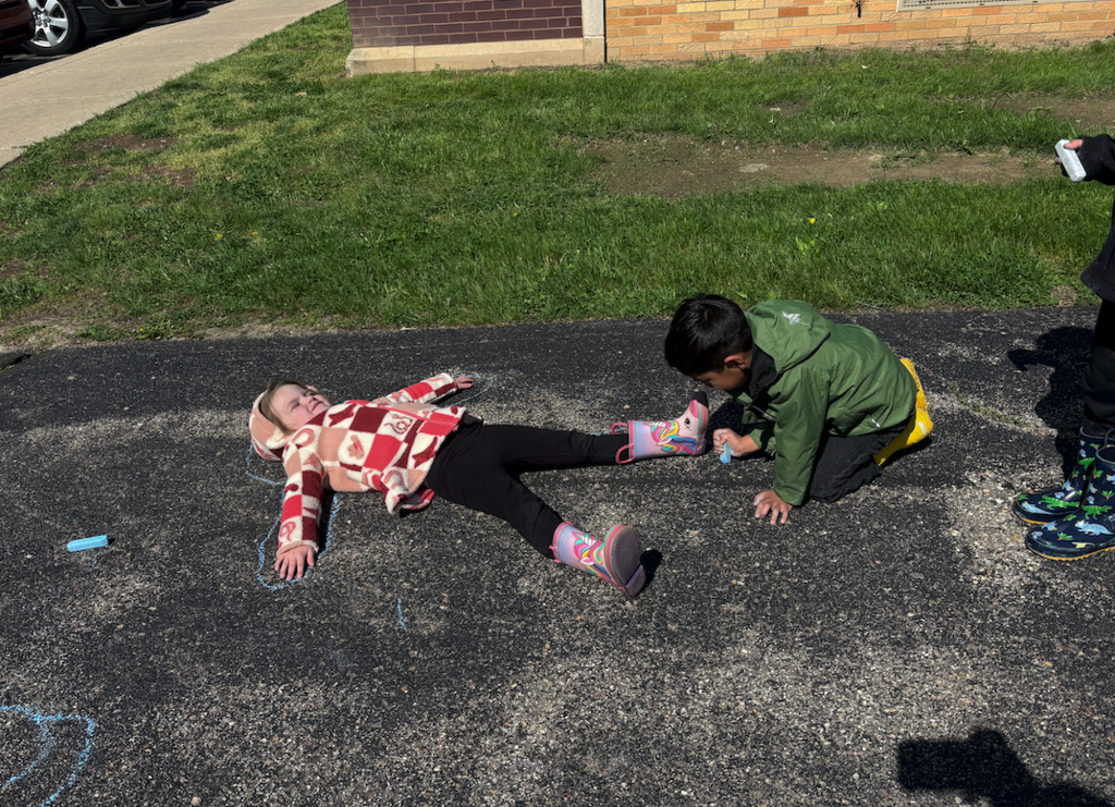 little boy tracing little girls outline with chalk