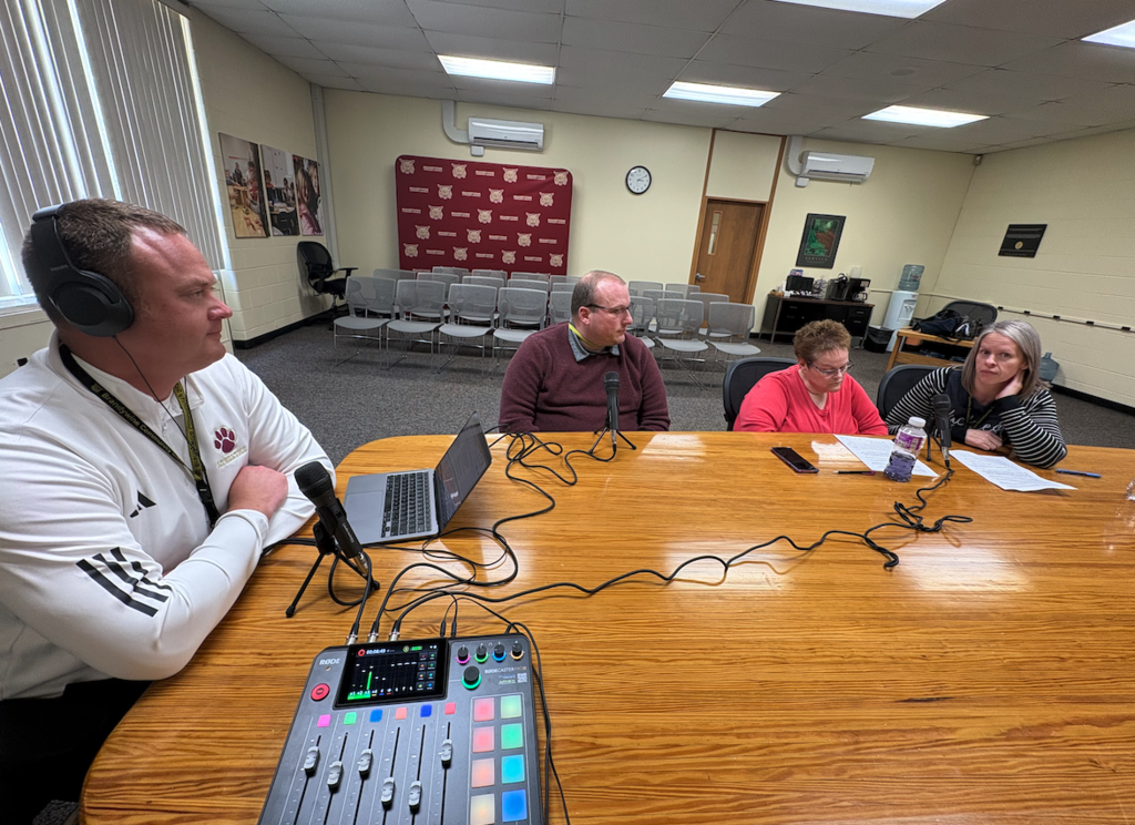 group of 3 teachers speaking on podcast, travis sitting at head of the table with headphones on