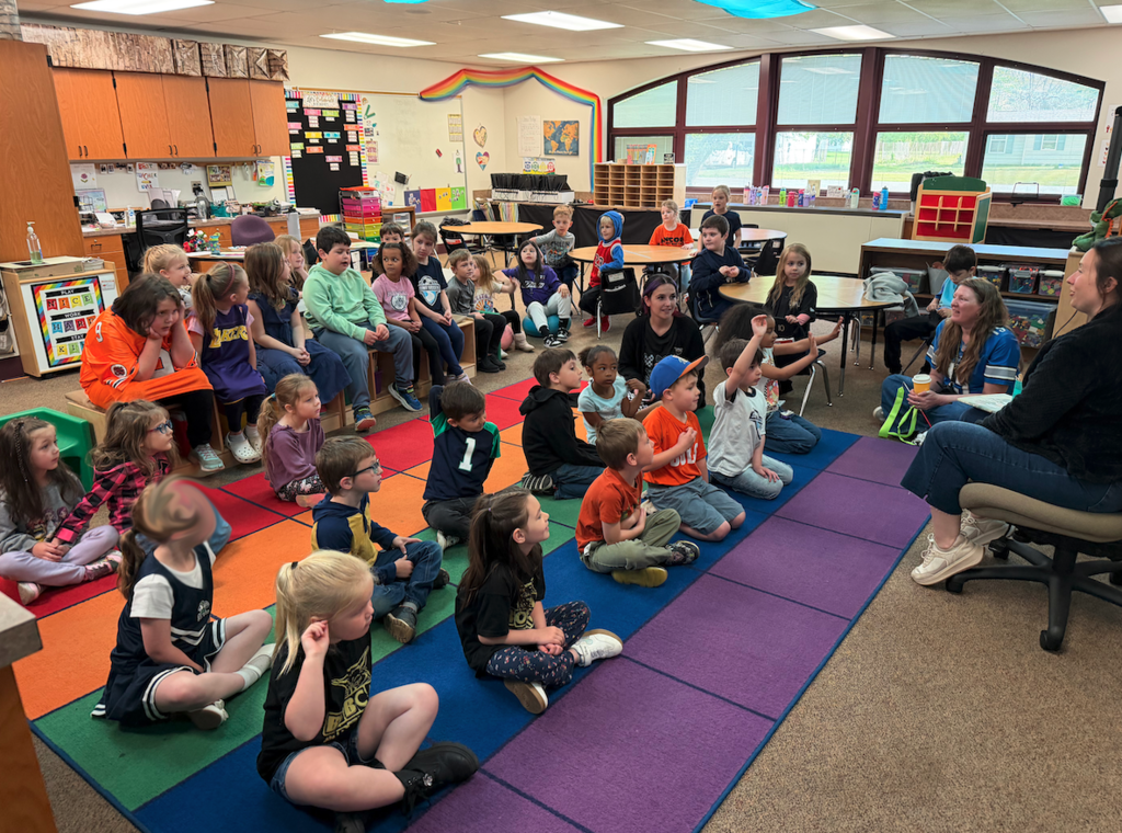students sitting on carpet listening to teacher