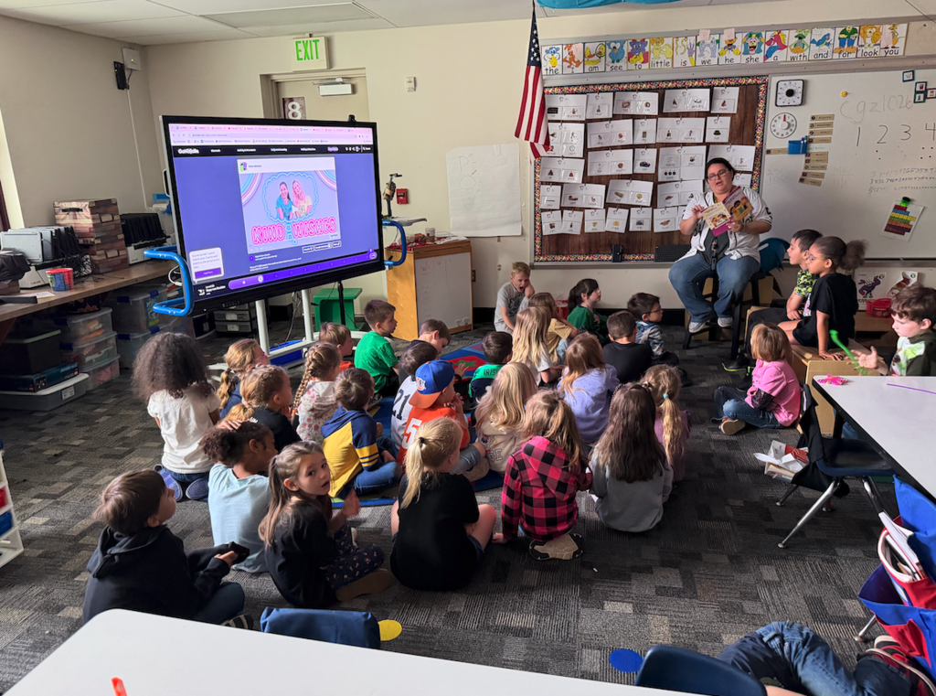 kids sitting in group on floor listening. to teacher read
