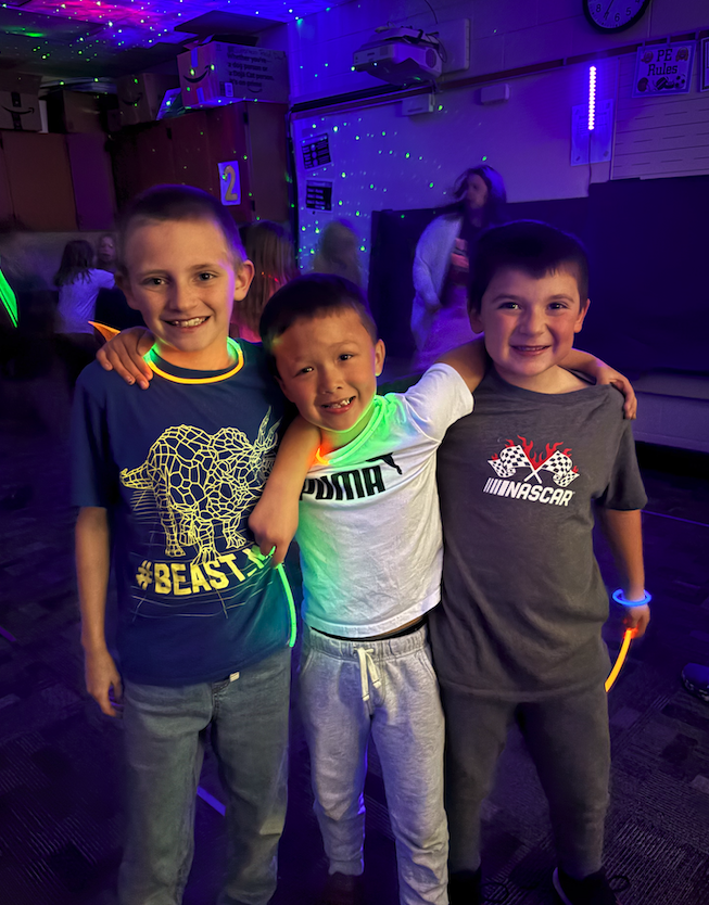 three boys wearing glow sticks, smiling with each other