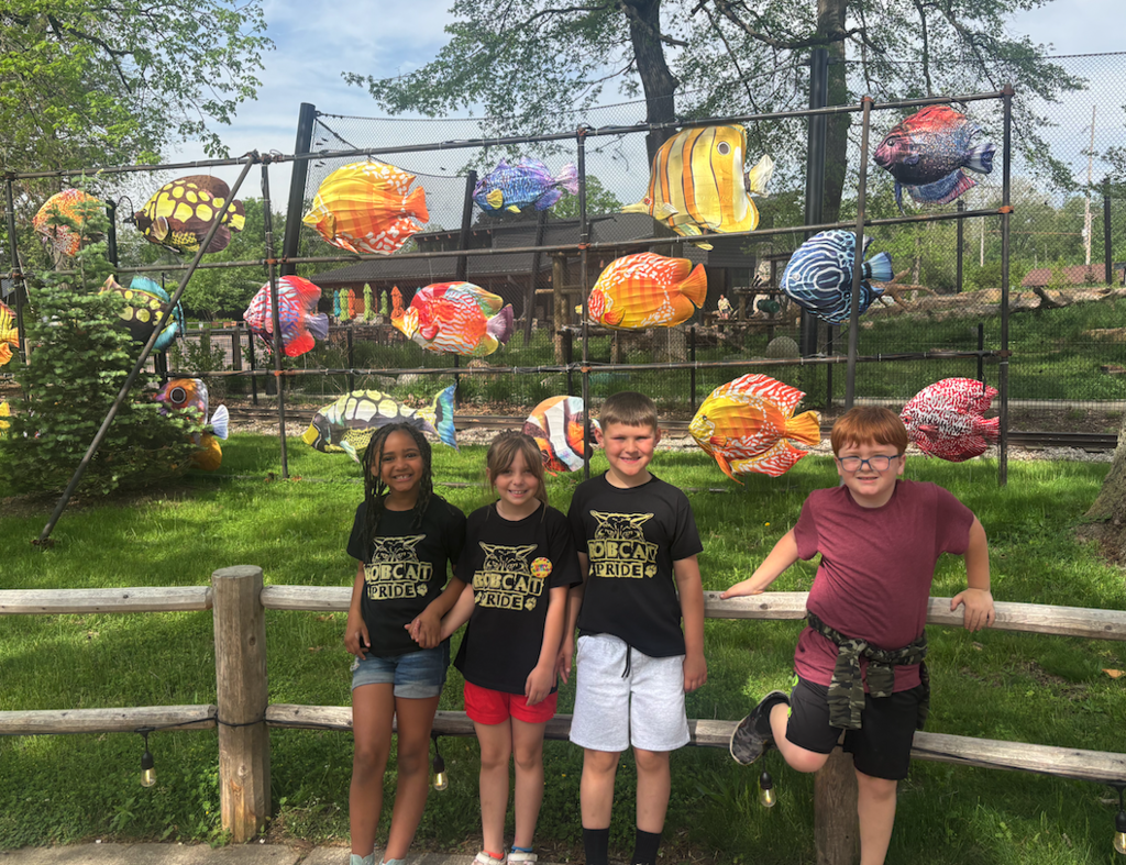 group of four students standing in front of a sculpture of fish in the background 