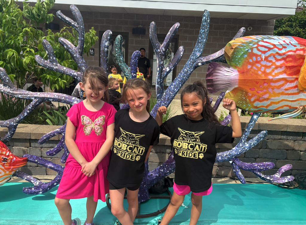 three young girls standing in front of a sculpture at the zoo