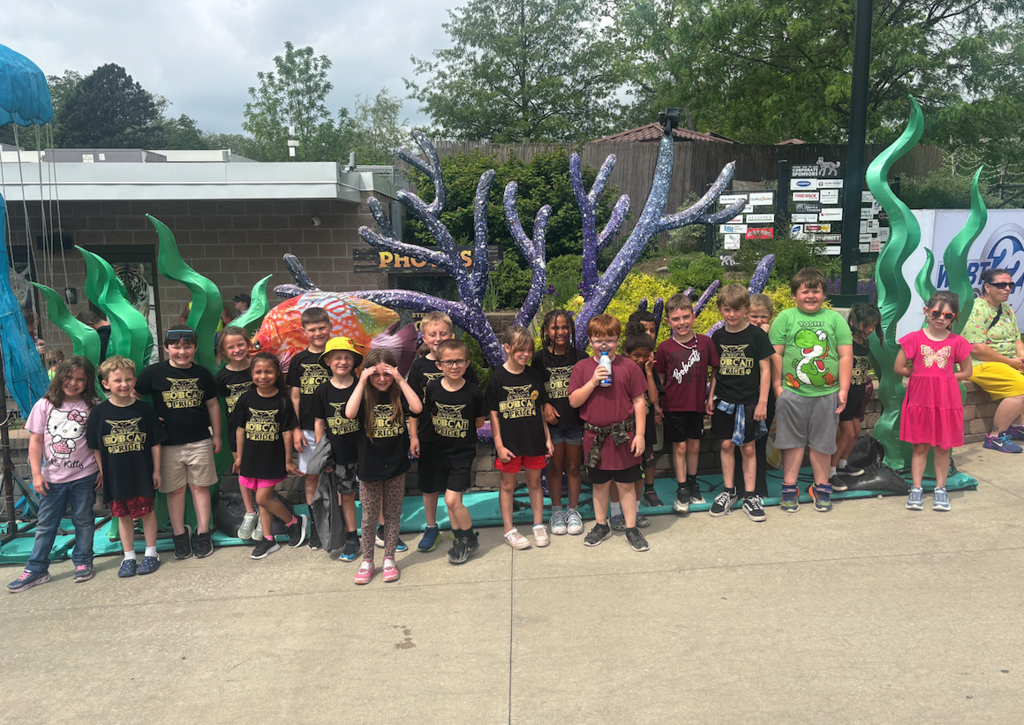 class of students standing in front of sculptures at the zoo