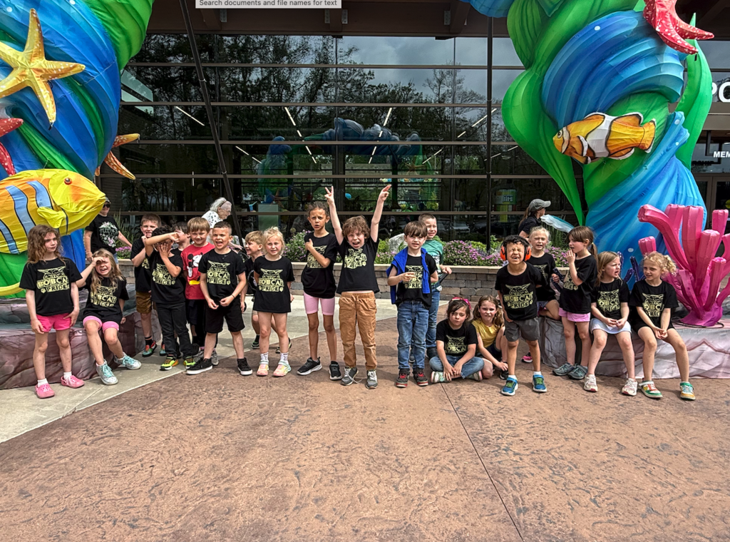 class of students standing in front of fish sculpture