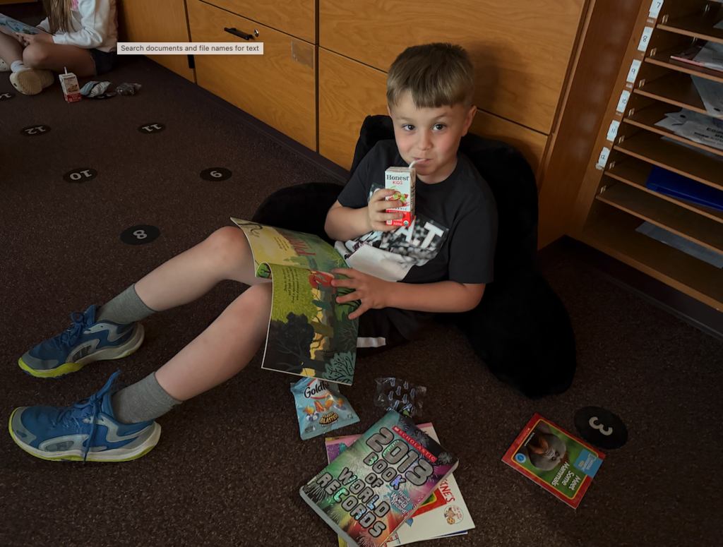 little boy sitting on the floor reading and drinking juice