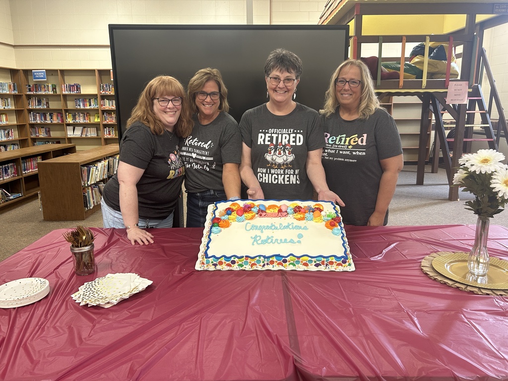 four women retirees smiling at camera, holding a cake that says "congratulations retirees"