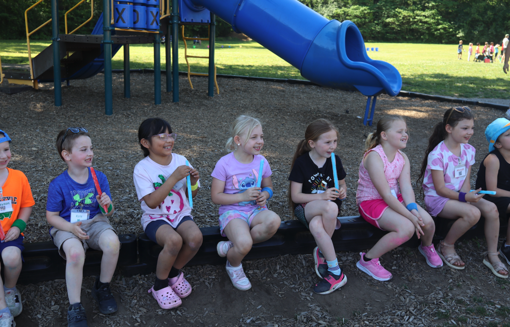 a group of little kids sitting on the playground, eating popsicles