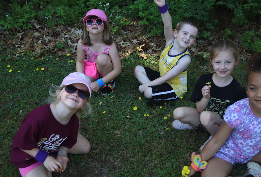 group of five kids sitting on ground looking at camera