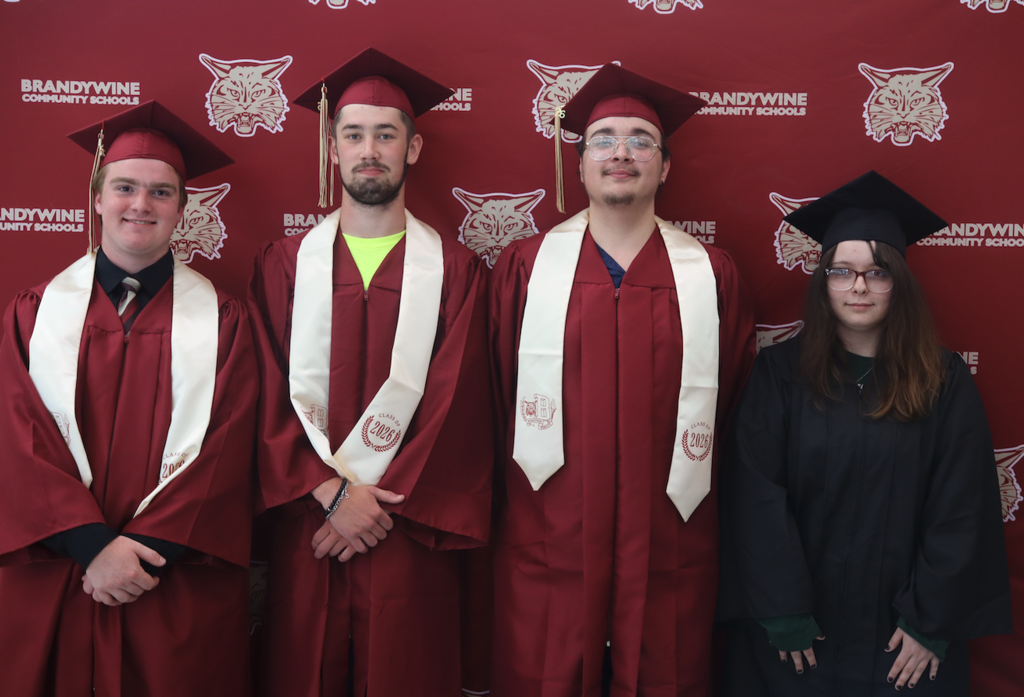 four graduates standing in front of backdrop in caps and gowns