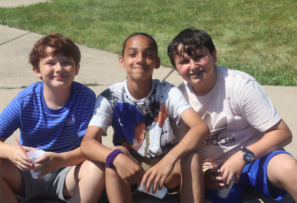 group of three boys sitting on sidewalk