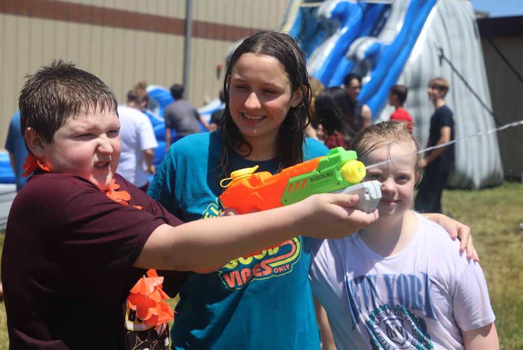 three kids standing together, one has a water gun