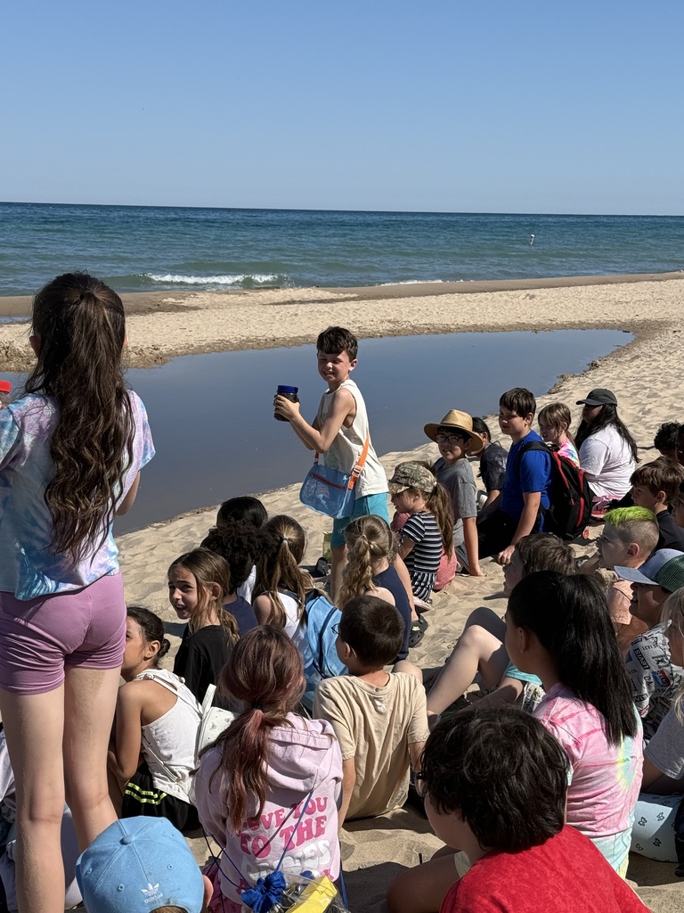 group of kids sitting on the beach, one young boy standing up looking at the camera