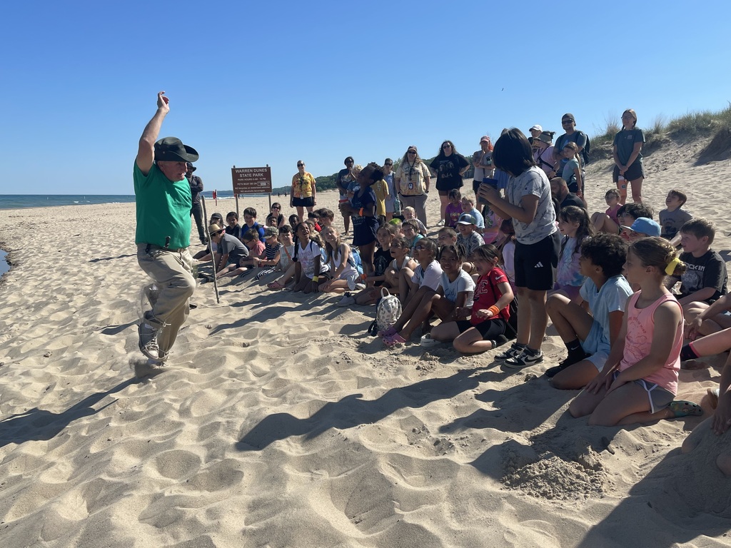 man showing class of students something on the beach