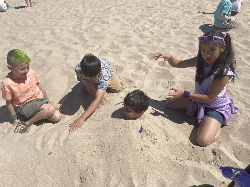 four kids burying one kid in the sand on the beach