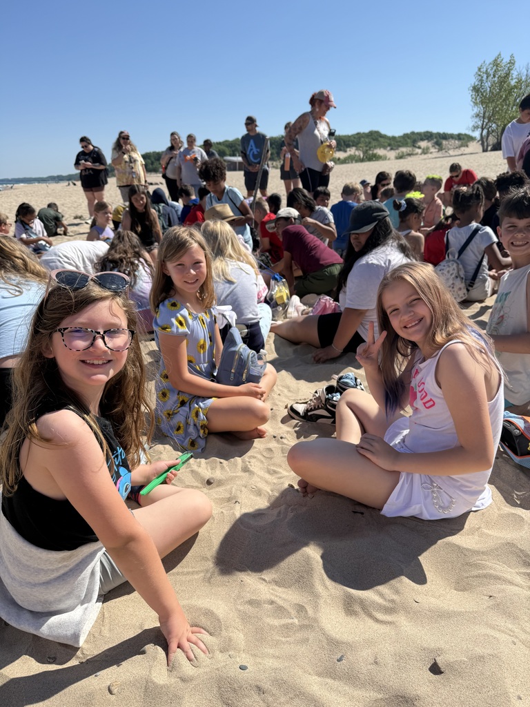 girls sitting on the beach, with classmates in the background
