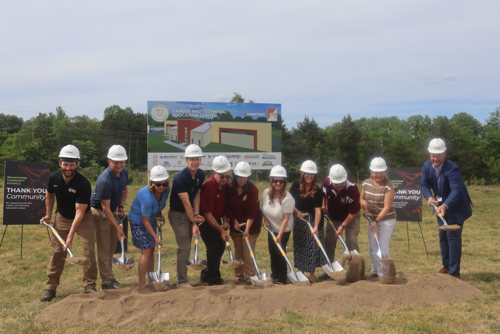 board members and administrators wearing hard hats and holding shovels