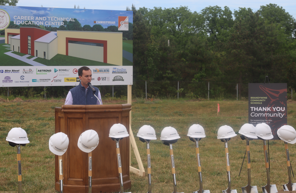 lee belding speaking at groundbreaking with hard hats and shovels in front of them