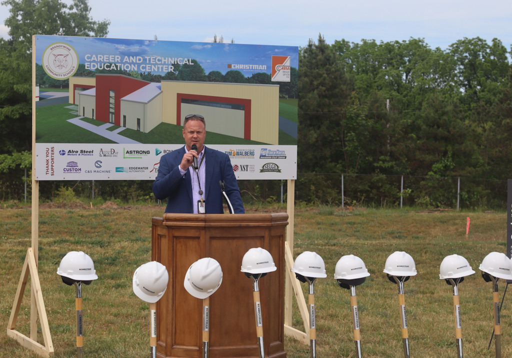 mr. walker speaking at groundbreaking with hard hats and shovels in front of them