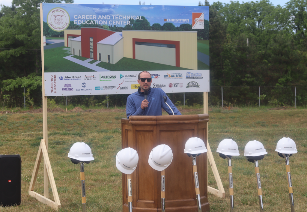 Anthony barnes from alro steel speaking at groundbreaking with hard hats and shovels in front of them