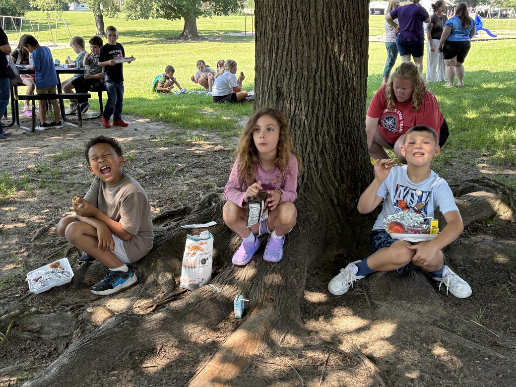 three kids sitting on the grass eating lunch