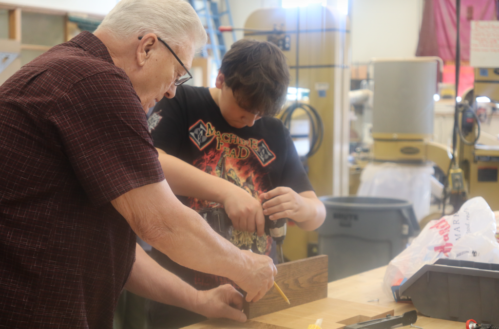 teacher helping student with wood piece