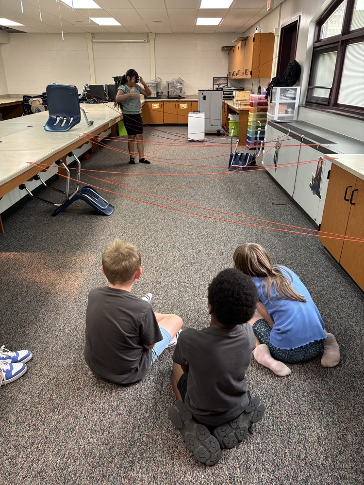 kids sitting on the ground with strings across the room