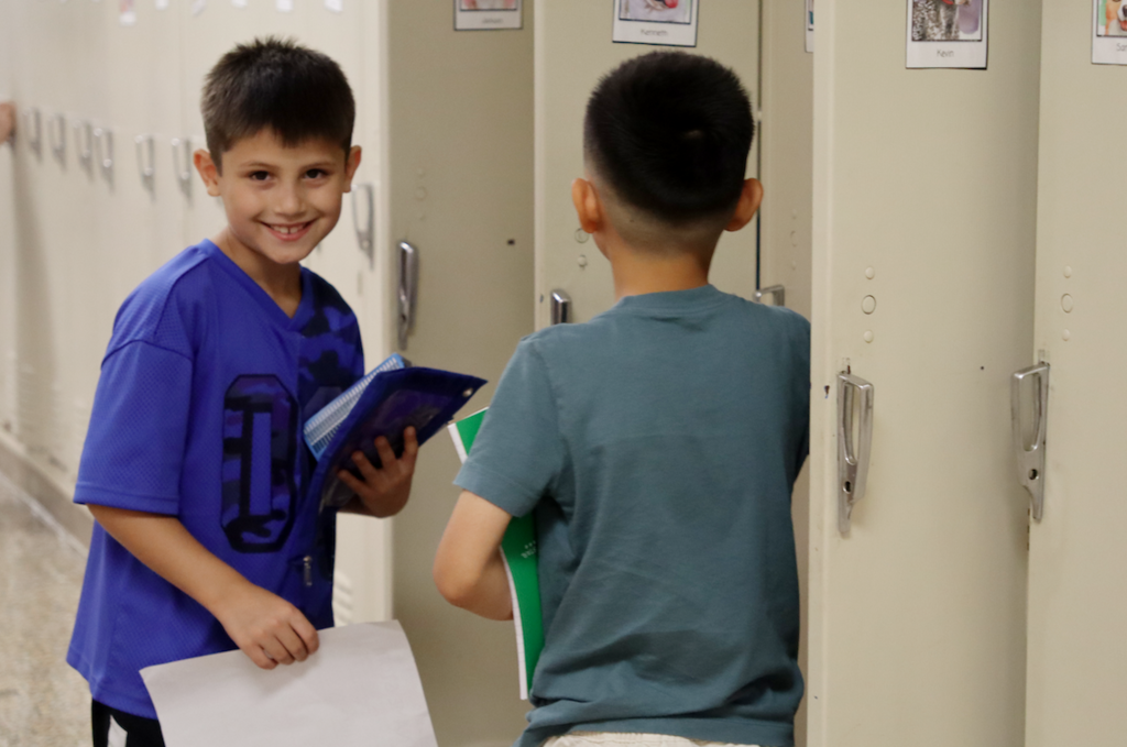 two little boys at their lockers, one smiling at the camera