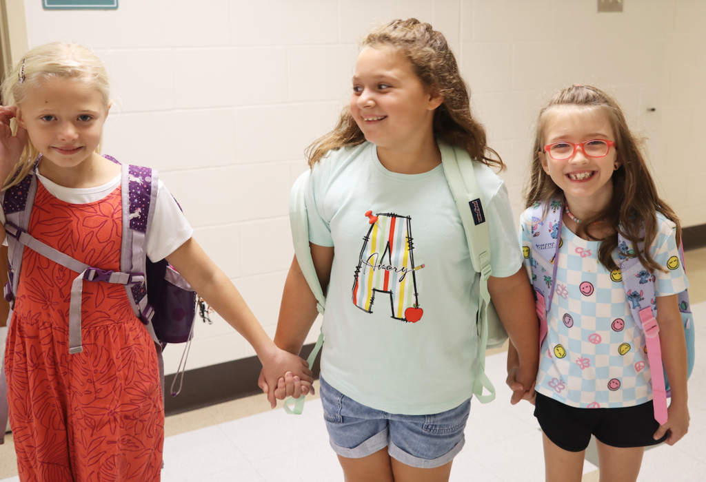 three little girls holding hands in the hallway